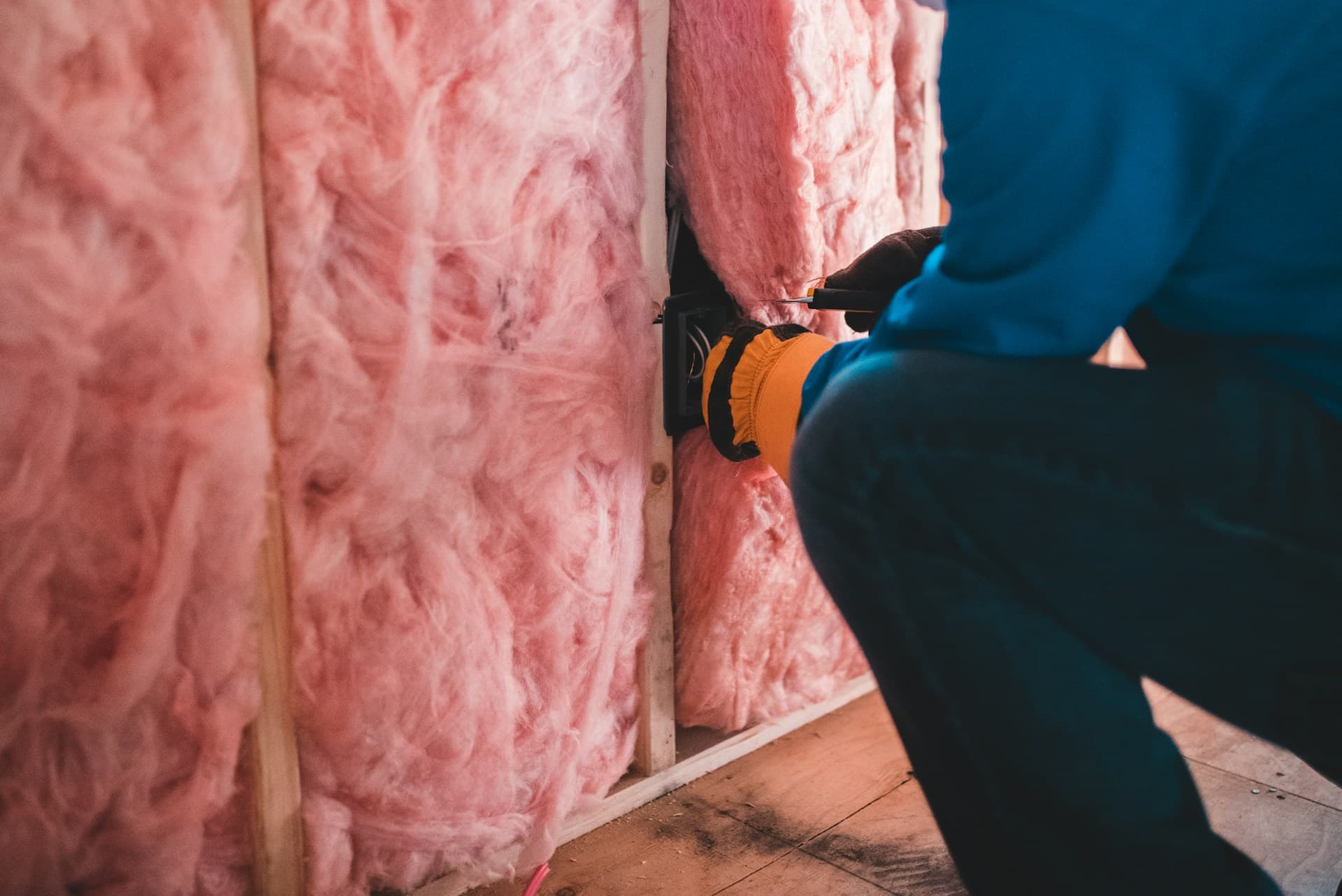 Insulation — a worker fitting batt insulation into a timber frame