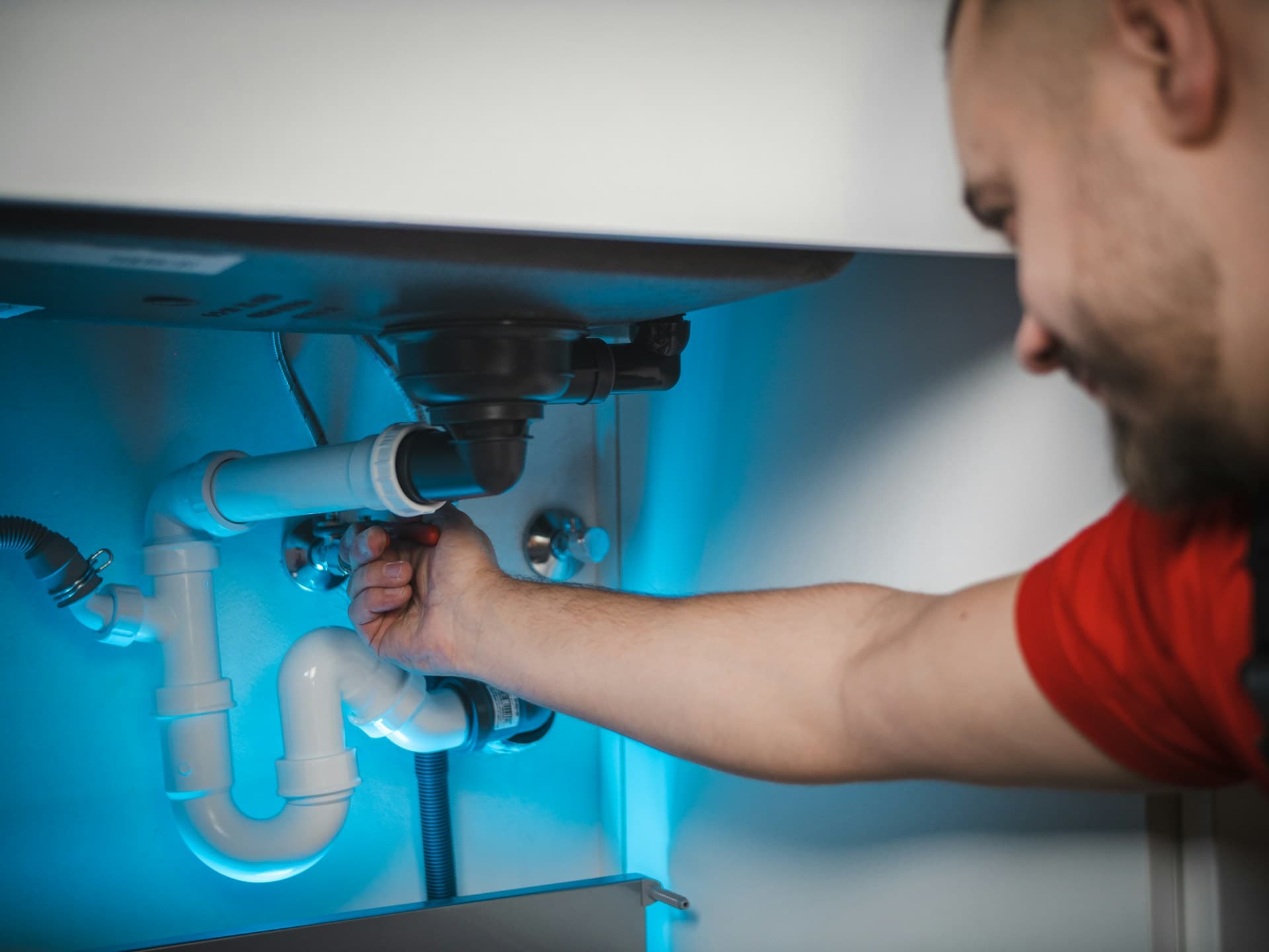 Plumbing — a plumber tightening pipework under a sink