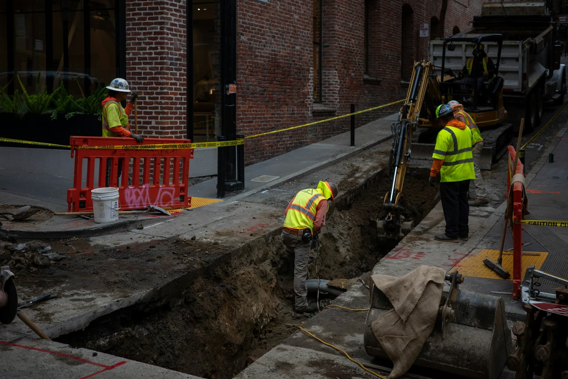 Hi-vis workers and excavator digging a trench in a city street