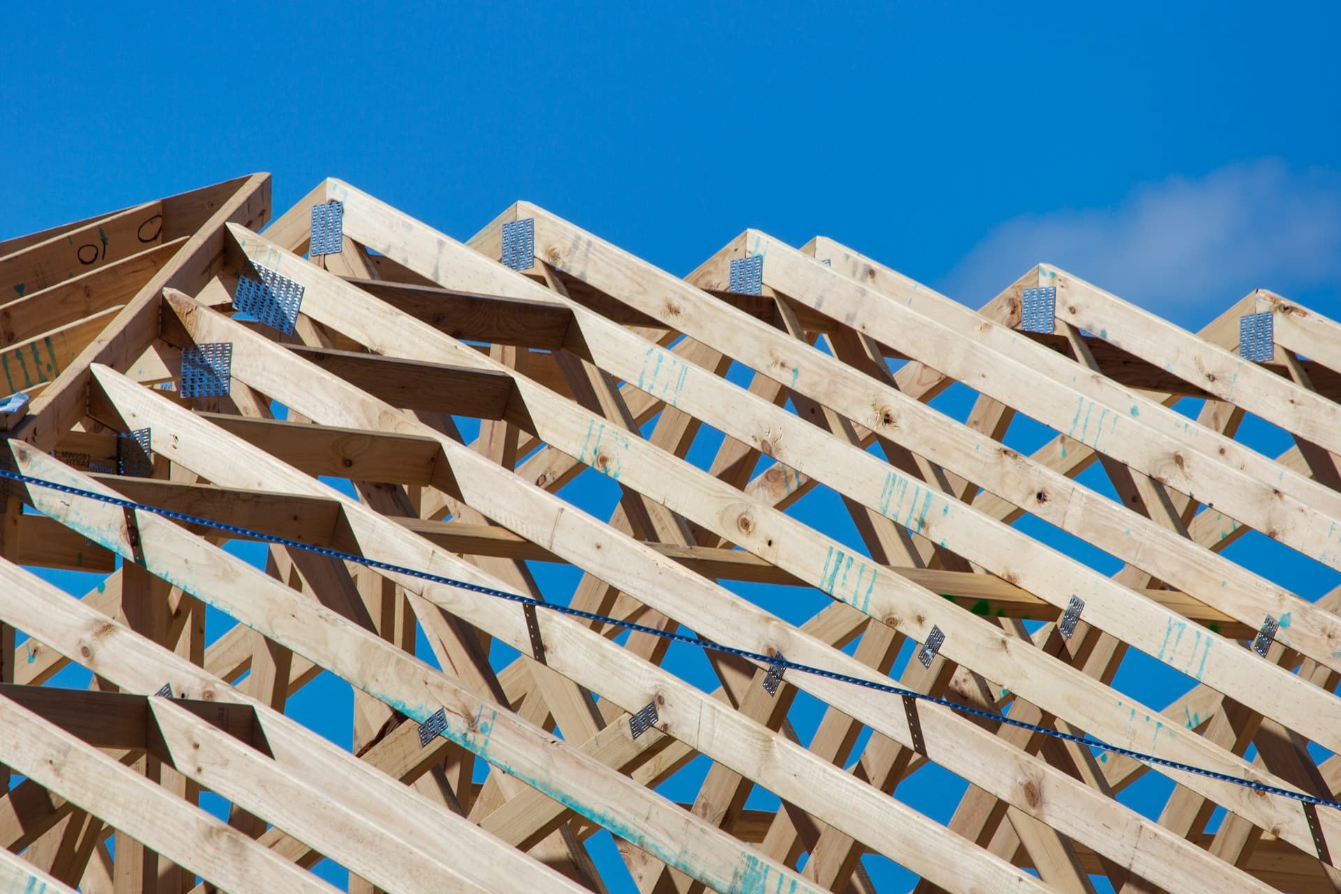 Timber roof trusses with metal gusset plates framed against a clear blue sky