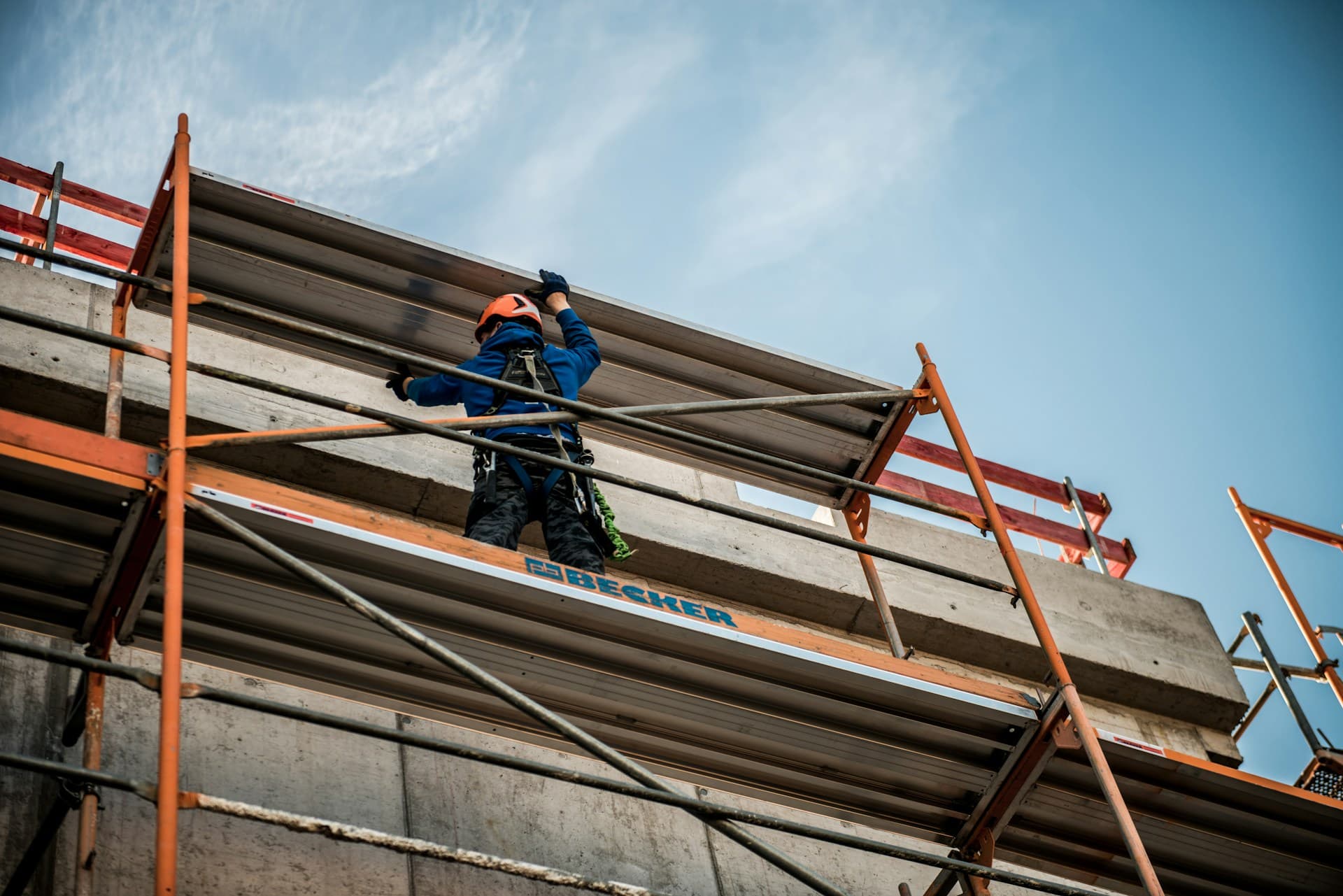 Working at heights — a worker on scaffolding handling a panel against the sky