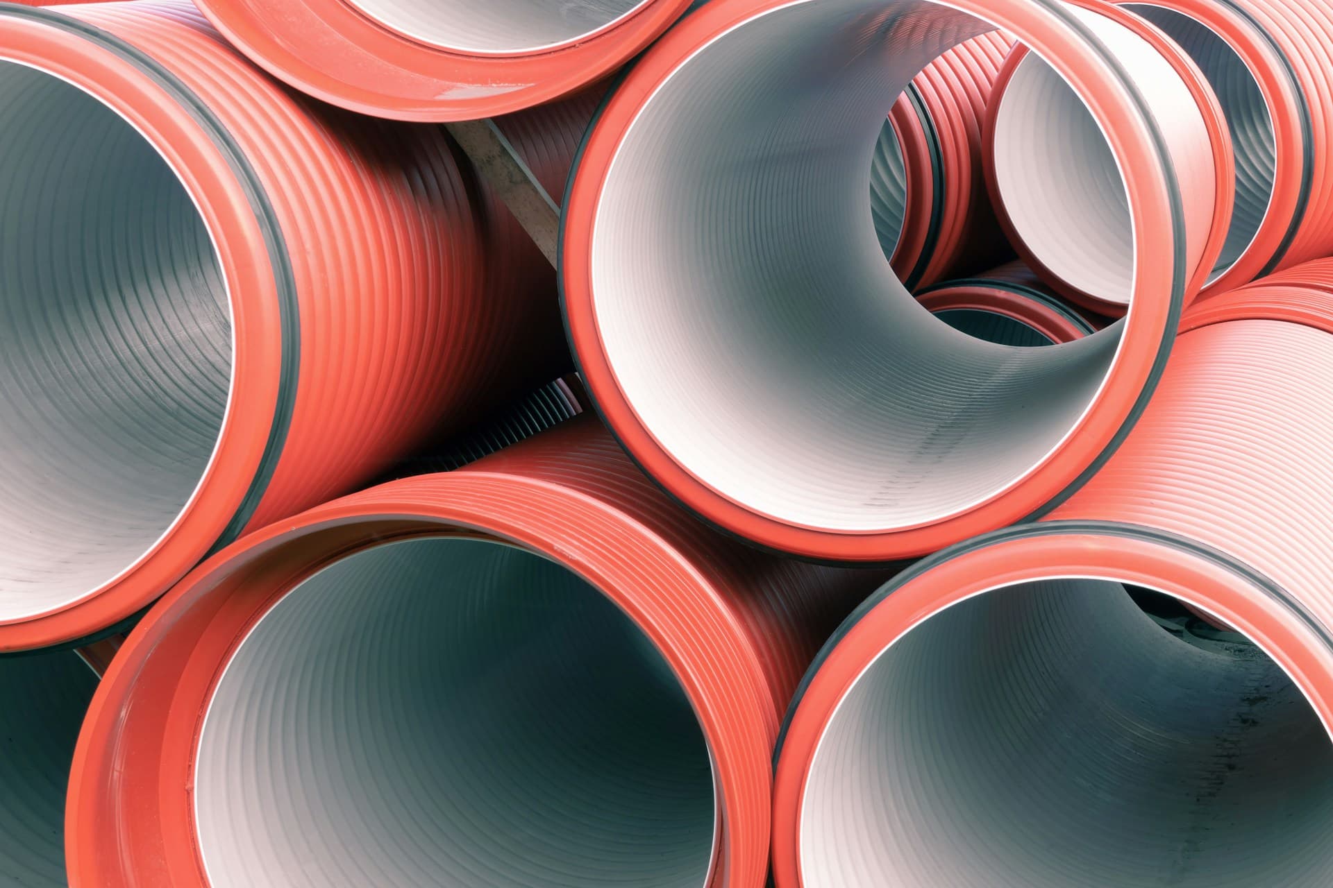 Stack of large orange and grey corrugated plastic drainage pipes