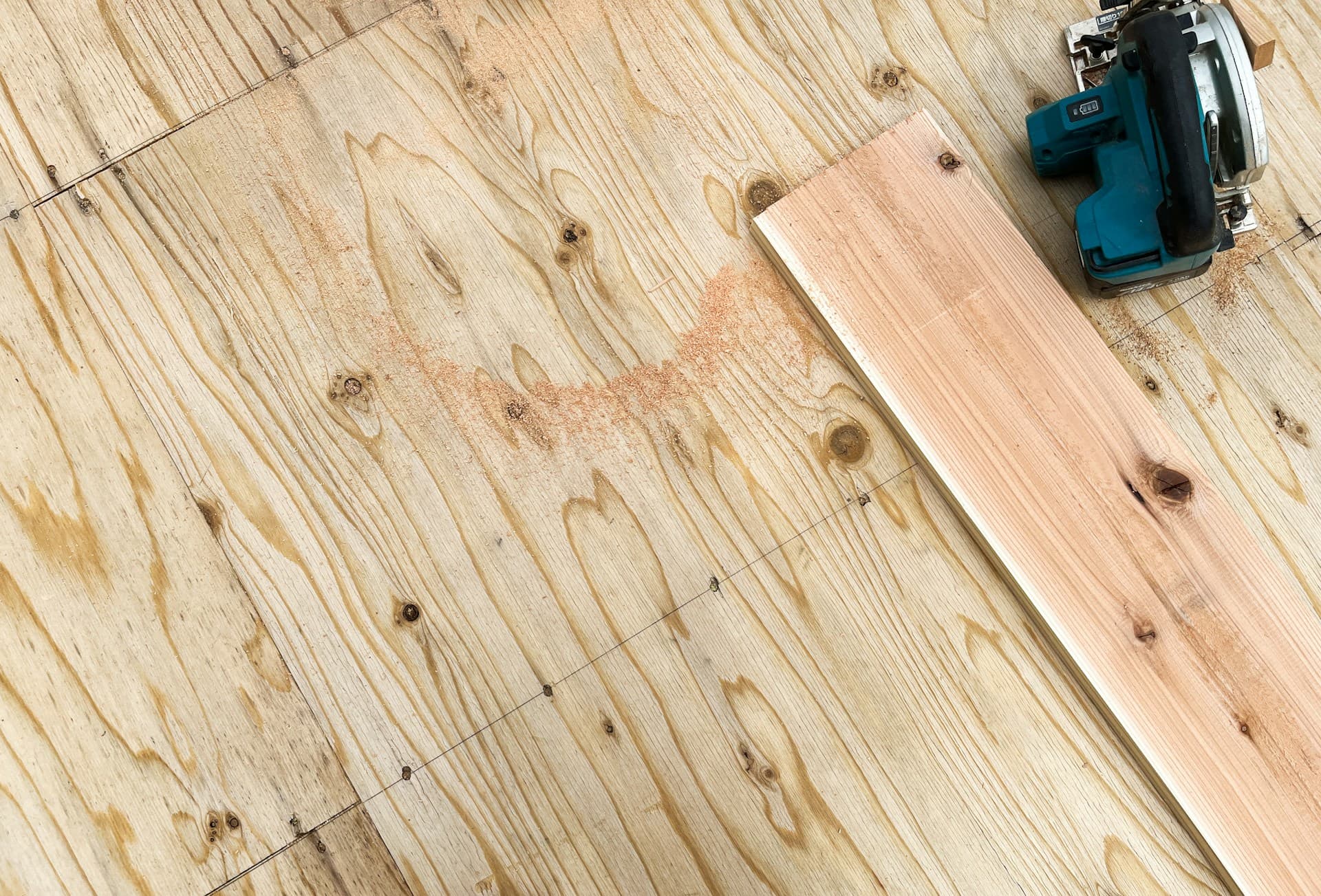 Circular saw and timber board on a plywood subfloor with sawdust